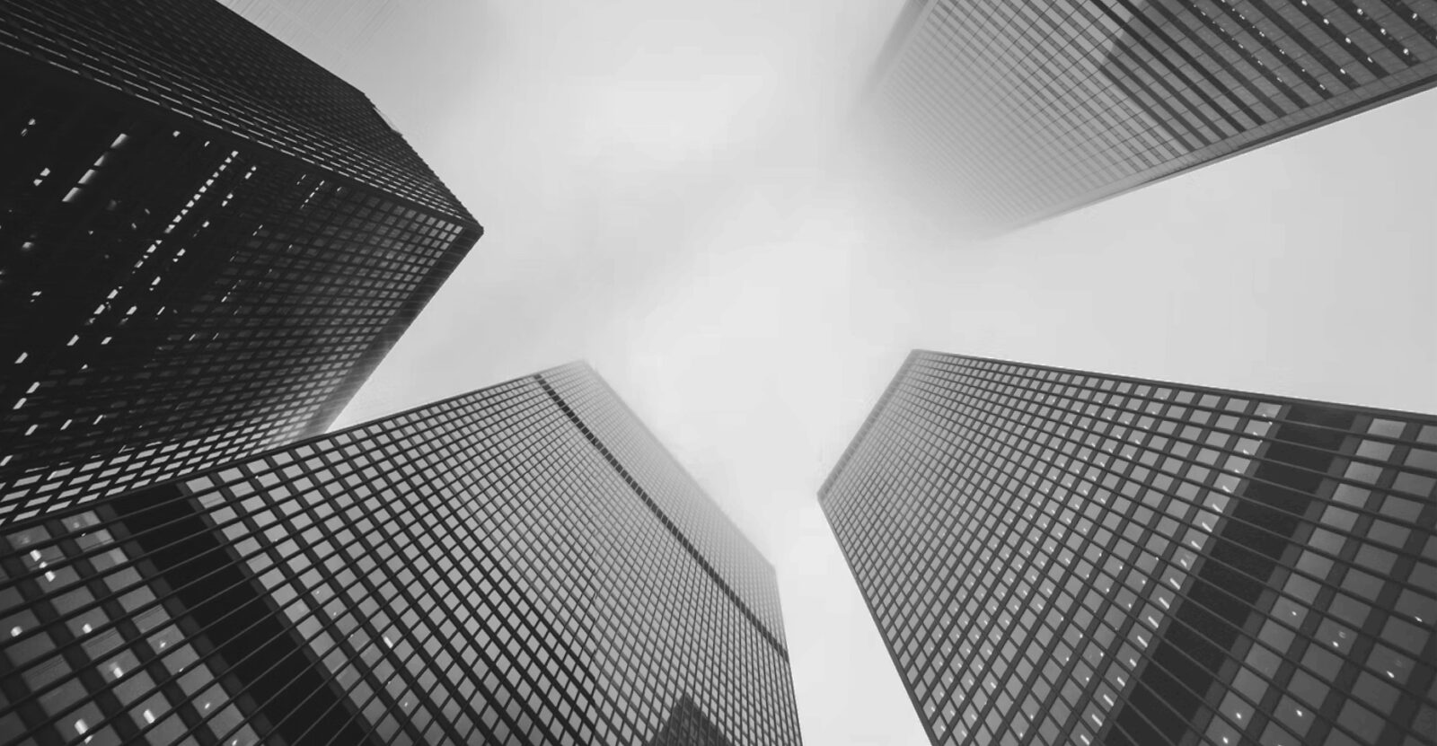 CloudMasonry Salesforce Consulting - Background Image - Upward view of modern skyscrapers in fog.