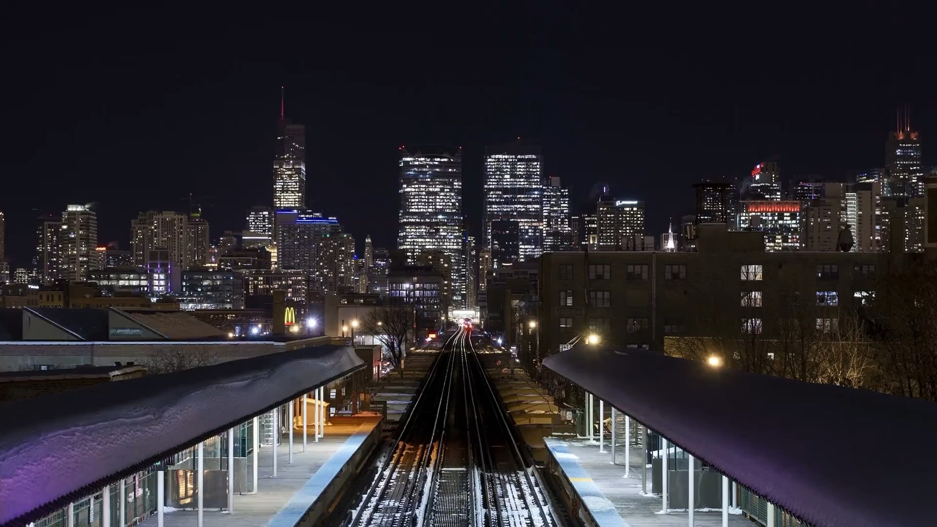Night view of city skyline over train tracks.